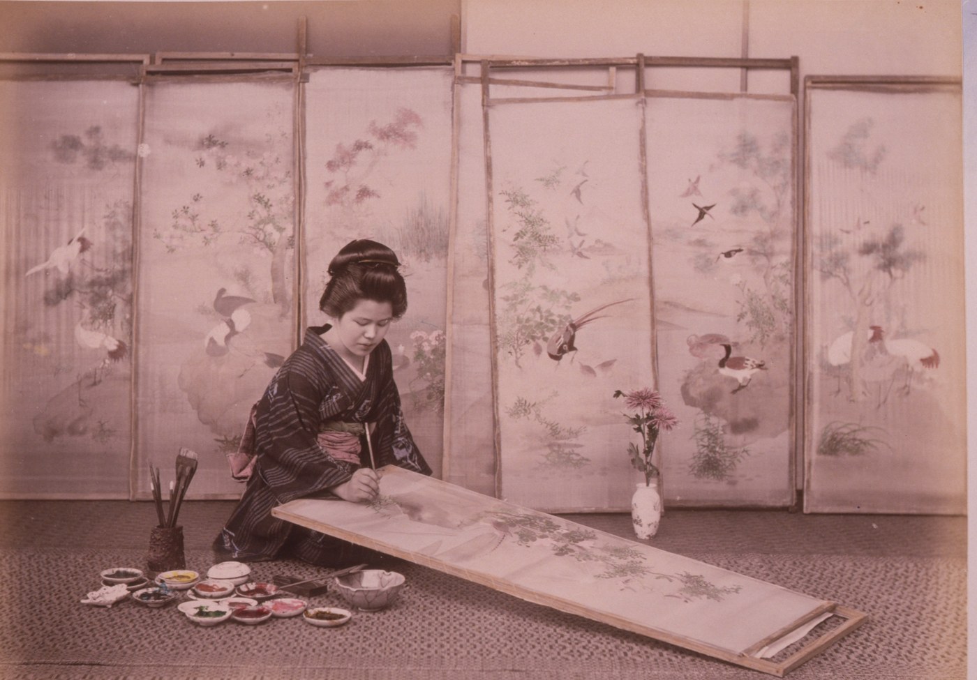 Placeholder portrait — a Meiji-era painter at work on a screen, brush in hand, dishes of pigment beside her